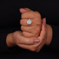 Hand wearing a diamond ring against a black background
