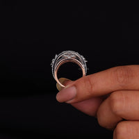 Hand holding a ring with intricate design against a black background
