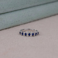 Silver ring with blue gemstones on a light gray surface, White & Blue Sapphire CZ Band – Round Stone Alternative Wedding Ring