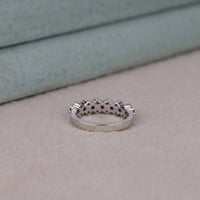 Silver ring with blue stones on a beige surface, Round Brilliant CZ Wedding Band – White & Blue Sapphire Alternative Eternity Ring
