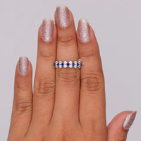 Hand wearing a silver ring with blue gemstones on a plain background, Round Cut White & Blue CZ Sapphire Ring – Modern Alternative Wedding Band