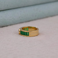 Gold ring with green gemstones on a light gray background
