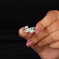 Hand holding a silver ring with floral design against a black background