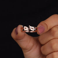 Rose gold ring with leaf design held between fingers against a black background