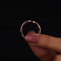 Rose gold hoop earring held between fingers against a black background