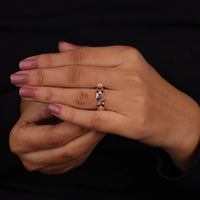 Hand wearing a silver ring with pink nail polish on a black background