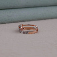 Stack of rose gold rings with diamond accents on a neutral background