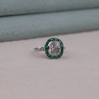 Ring with a central gemstone and emerald accents on a neutral background