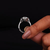 Silver ring with a large diamond held by a hand against a black background