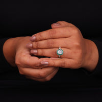 Hand wearing a ring with a green gemstone on a black background