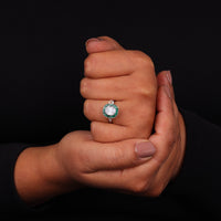 Hand holding a ring with a green gemstone against a black background