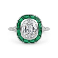 Diamond ring with emerald green gemstones on a white background