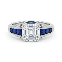 Elegant ring with emerald-cut diamond and blue gemstones on a white background