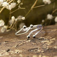 Silver crab-shaped ring with black accents on a wooden surface with dried flowers in the background