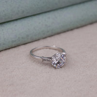 Silver ring with a large diamond on a light gray surface, moissanite jewelry for special occasions, round cut moissanite seven stone ring, claw setting moissanite engagement ring, seven stone moissanite wedding ring, moissanite anniversary ring for women