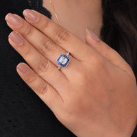 Close-up of a hand wearing a ring with a blue gemstone on a black background, geometric art deco target ring, asscher cut milgrain wedding ring, blue sapphire baguette engagement ring,