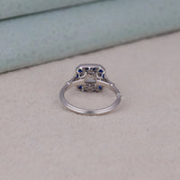 Silver ring with blue gemstones on a light gray surface, heirloom inspired sapphire engagement ring, custom sapphire and asscher ring, blue sapphire baguette side stone ring