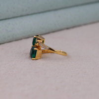 Gold ring with green gemstones on a light gray surface, Green CZ Bypass Ring, Two Stone CZ Engagement Ring, Unique Asscher Cut Toi Et Moi Ring, Affordable CZ Wedding Jewelry