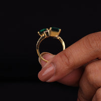 Gold ring with green gemstones held by a hand against a black background, Dainty Asscher Cut CZ Engagement Band, Timeless Toi Et Moi Engagement Jewelry, Symbolic Two Stone CZ Ring
