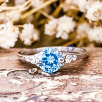 Silver ring with a blue gemstone on a wooden surface with flowers in the background