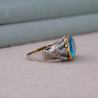 Ring with a blue gemstone and gold accents on a neutral background, Cool Superhero Inspired Statement Ring, Poseidon Ocean King Ring For Collectors, Modern Streetwear Jewelry With Aqua Man Theme