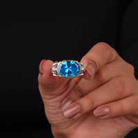 Hand holding a ring with a blue gemstone against a black background