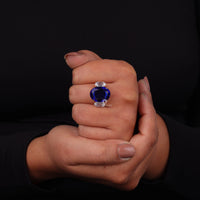 Hand holding a ring with a blue gemstone against a black background, Elegant Oval Blue Sapphire & CZ Three Stone Wedding Engagement Ring
