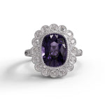 Ring with a purple gemstone and diamond-studded halo on a white background