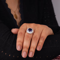 Close-up of a hand wearing a ring with a blue gemstone on a dark background, Vintage Cushion Blue Sapphire Halo Cocktail Ring with Round White CZ