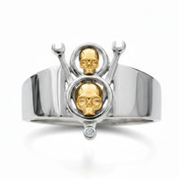 Silver ring with gold skull designs and a diamond on a white background