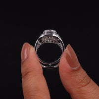 Close-up of a hand holding a silver ring with a large central gemstone against a black background, Sustainable Art Deco Wedding Band, Timeless Moissanite Halo Ring Set, Vintage Inspired Bridal Jewelry,