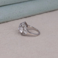 Silver ring with a large diamond and smaller diamonds on a light gray surface, women’s antique art deco style wedding jewelry, round cut cubic zirconia ring for engagement gift.