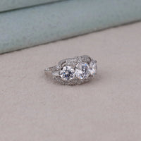 Silver ring with multiple gemstones on a light gray surface, art deco inspired promise ring with CZ stones, classic three stone CZ engagement ring