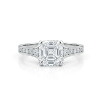 Diamond ring with a central emerald-cut diamond and smaller diamonds on the band against a white background