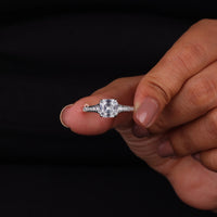 Diamond ring held between fingers against a black background