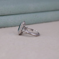 Silver ring with a green gemstone on a light gray surface