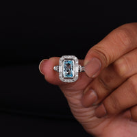 Ring with a blue gemstone held between fingers against a black background