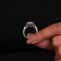 Silver ring held between fingers against a black background