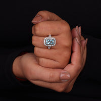 Hand holding a ring with a blue gemstone and diamond accents against a black background