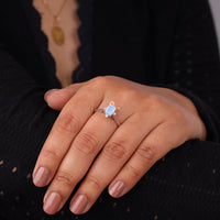 Hand wearing a ring with a blue gemstone against a dark background, Emerald Cut Rainbow Moonstone With White Round CZ Five Stone Minimalist Ring, Rainbow Moonstone Emerald Cut Engagement Ring