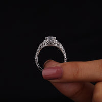 Silver ring with intricate design held by a hand against a black background