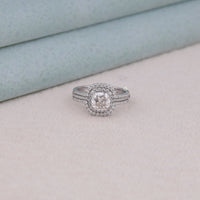 Silver ring with gemstone on a light gray surface, Conflict Free Moissanite Wedding Jewelry, Elegant Halo Guard Bridal Set For Women, Affordable Moissanite Wedding Ring Set, Cushion Cut Moissanite Promise Ring