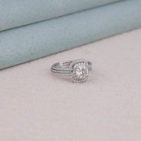 Silver ring with a large central gemstone and smaller stones on a light gray surface, Bridal Guard Enhancer Band With Moissanite, Eco Friendly Cushion Moissanite Wedding Jewelry, Unique Cushion Halo Bridal Set