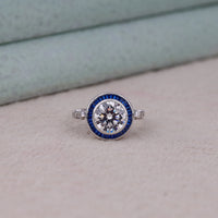 Silver ring with a diamond and blue gemstone setting on a light gray surface, Blue Sapphire CZ Halo Ring – Vintage Target Style Art Deco Jewelry