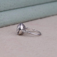 Silver earring on a light gray surface with a neutral background, Vintage Blue Sapphire Target Ring – Round CZ Art Deco Halo Jewelry Gift