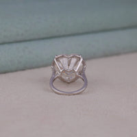 Silver ring with a heart-shaped stone on a neutral background, Halo Heart Moissanite Bridal Jewelry, Symbolic Heart Cut Ring For Engagement, Modern Halo Style Moissanite Wedding Band