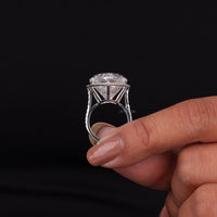 Silver ring with a large diamond held by a hand against a black background, Heart & Round Moissanite Halo Engagement Ring, Romantic Heart Cut Moissanite Proposal Ring, Unique Heart Shaped Bridal Jewelry