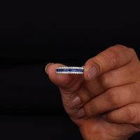 Hand holding a diamond ring with blue gemstones against a black background