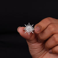 Hand holding a diamond ring with a star-like design against a black background