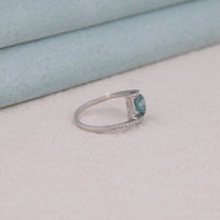 Silver ring with a green gemstone on a light gray surface